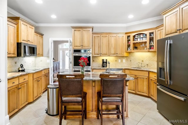 kitchen featuring a kitchen island with sink, appliances with stainless steel finishes, tasteful backsplash, a sink, and light stone counters