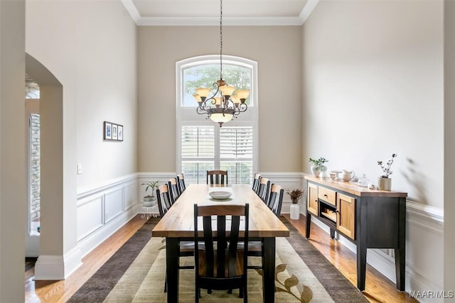 dining area featuring arched walkways, dark wood finished floors, a notable chandelier, and ornamental molding