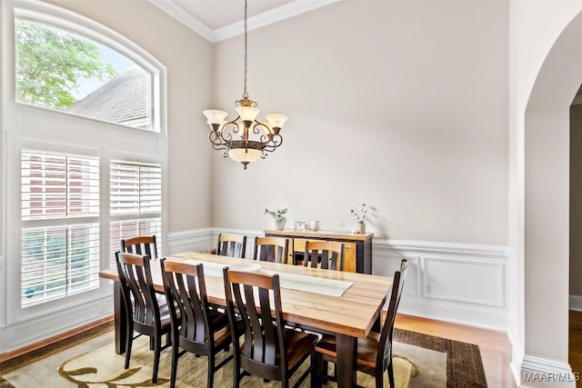 dining space with crown molding, a notable chandelier, wainscoting, arched walkways, and wood finished floors