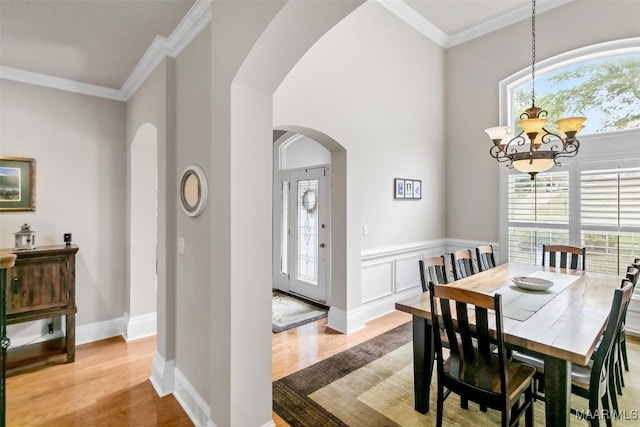 dining area with arched walkways, light wood-style flooring, a notable chandelier, and a wealth of natural light