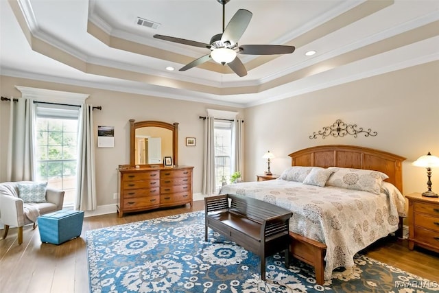 bedroom featuring multiple windows, ornamental molding, a tray ceiling, and wood finished floors