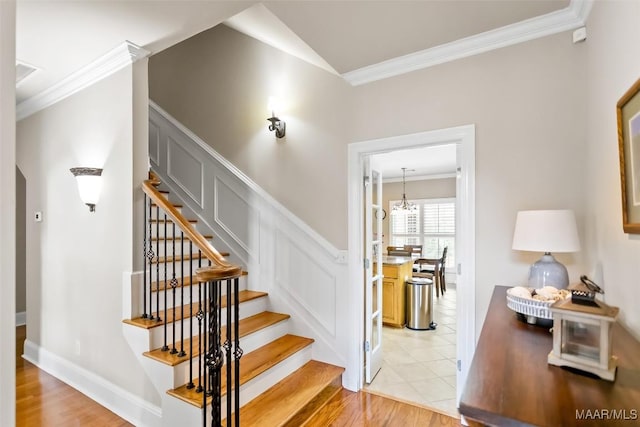 stairway with crown molding, a decorative wall, wood finished floors, and a wainscoted wall