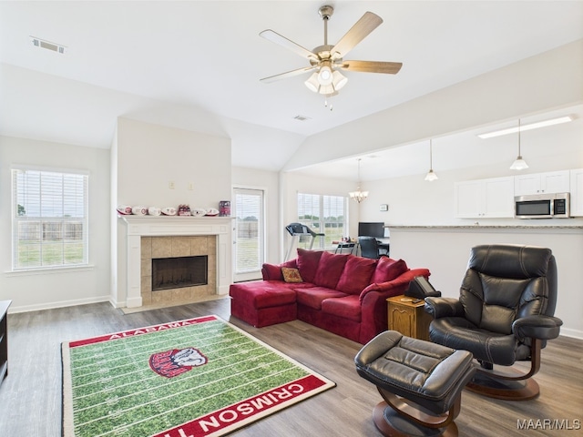 living area featuring a tiled fireplace, ceiling fan with notable chandelier, wood finished floors, and lofted ceiling
