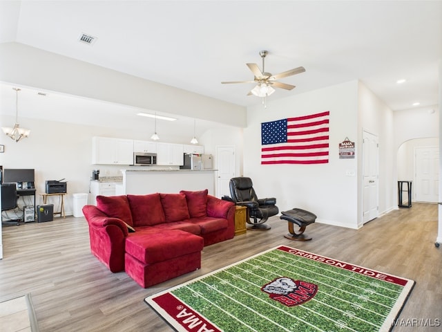 living room with arched walkways, ceiling fan with notable chandelier, light wood finished floors, and visible vents