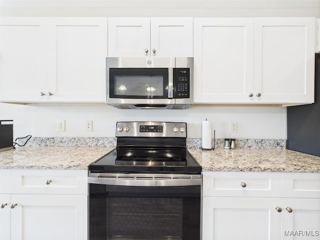 kitchen with stainless steel appliances, light stone countertops, and white cabinetry