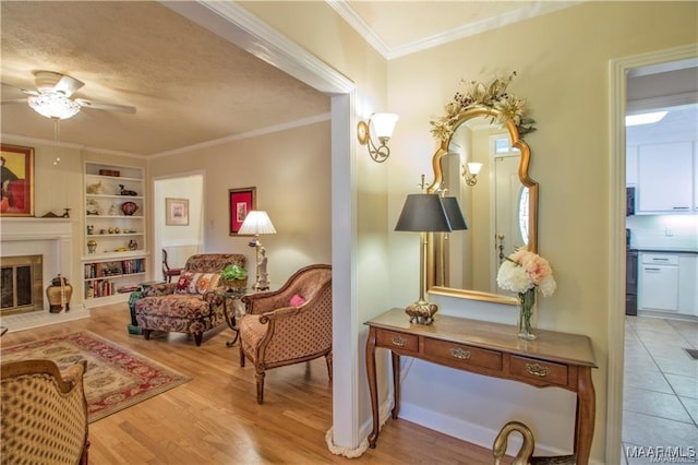 908 W Tuskeena St, Wetumpka, AL 36092 - sitting room featuring a glass covered fireplace, built in shelves, a ceiling fan, light wood-type flooring, and ornamental molding
