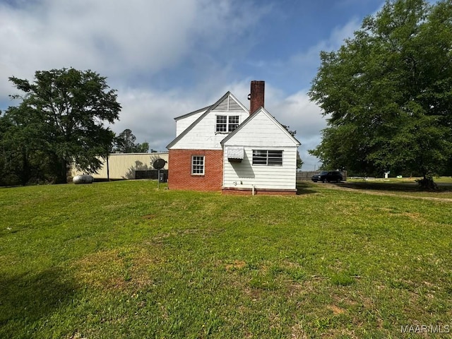 back of house featuring a lawn, brick siding, and a chimney