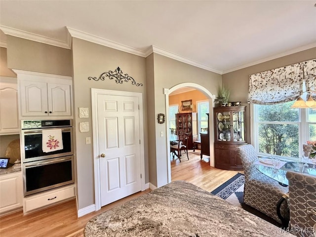 interior space featuring crown molding, arched walkways, double oven, and light wood finished floors