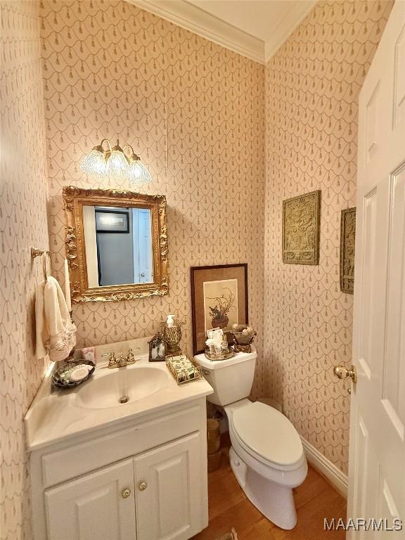 half bathroom with vanity, ornamental molding, toilet, and wallpapered walls
