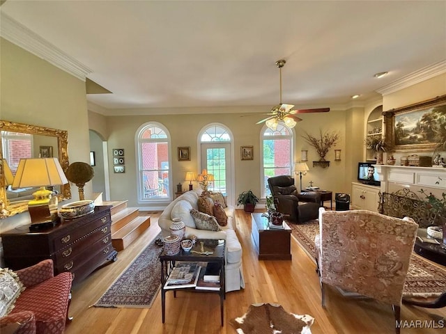 living room featuring crown molding, light wood finished floors, ceiling fan, and a wealth of natural light