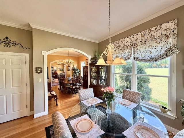 dining area with crown molding, an inviting chandelier, arched walkways, light wood-style flooring, and baseboards