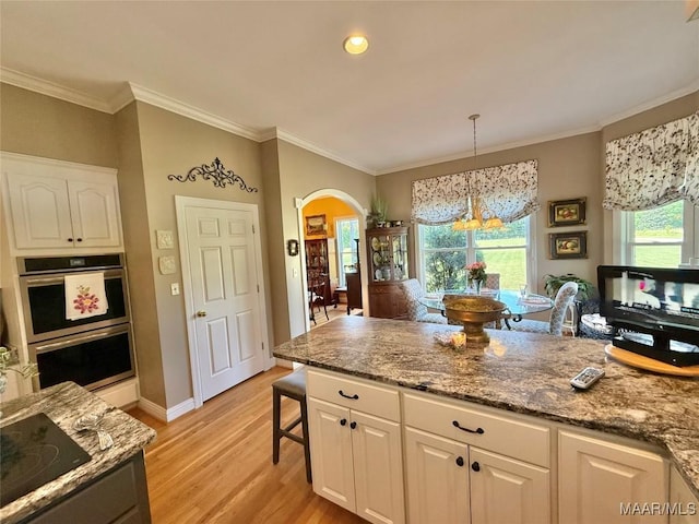 kitchen with stainless steel double oven, light wood-style flooring, arched walkways, and white cabinets
