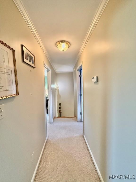 corridor featuring baseboards, ornamental molding, and light carpet
