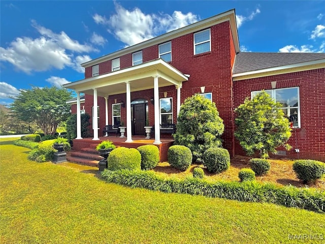 rear view of house featuring a yard, a porch, and brick siding