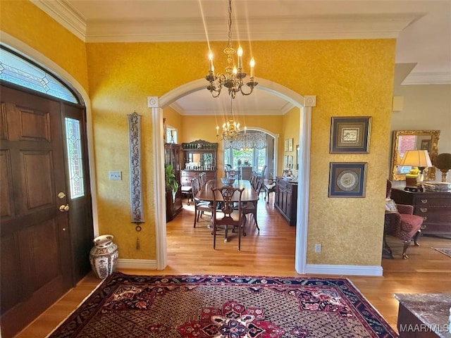 entryway with crown molding, arched walkways, wood finished floors, and a notable chandelier