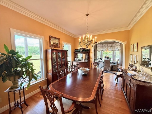 dining space featuring an inviting chandelier, arched walkways, light wood-style flooring, baseboards, and ornamental molding