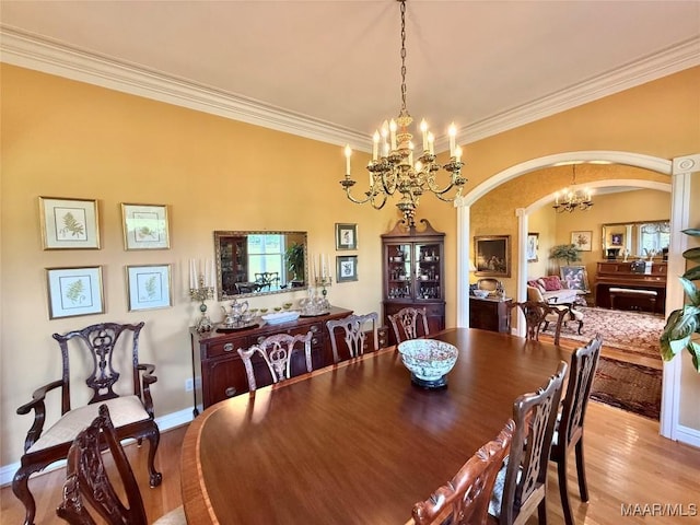 dining room with crown molding, a notable chandelier, arched walkways, light wood-style flooring, and baseboards