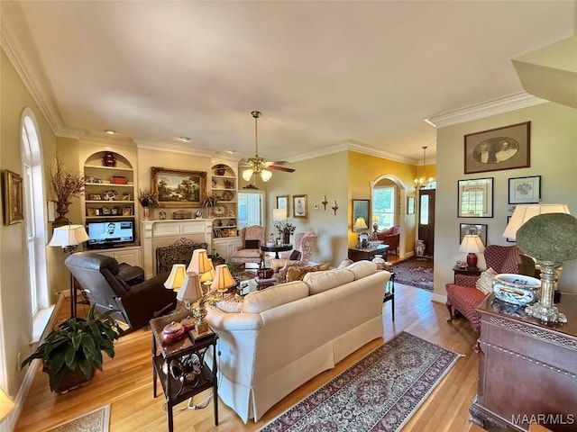 living room featuring ornamental molding, ceiling fan with notable chandelier, wood finished floors, and built in shelves
