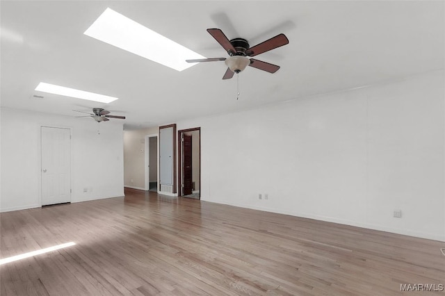 empty room featuring ceiling fan, a skylight, baseboards, and light wood-type flooring