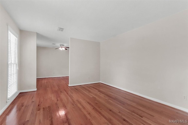 unfurnished room featuring baseboards, a ceiling fan, wood finished floors, and visible vents