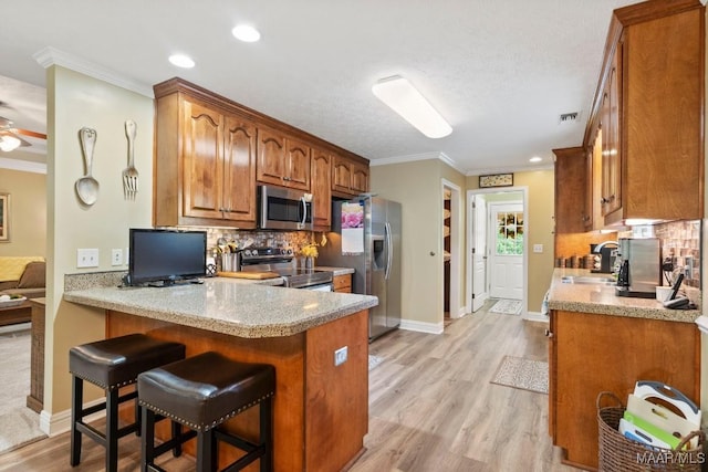 kitchen featuring appliances with stainless steel finishes, brown cabinetry, a peninsula, tasteful backsplash, and ornamental molding
