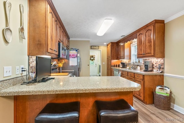 kitchen featuring appliances with stainless steel finishes, light wood-style flooring, a peninsula, backsplash, and ornamental molding