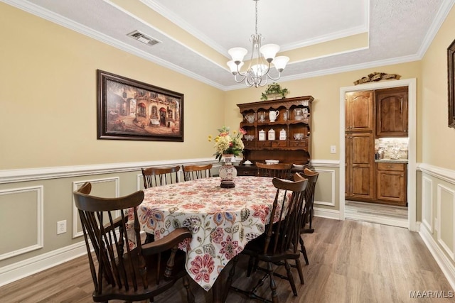 dining space featuring visible vents, a raised ceiling, a chandelier, light wood-style floors, and a decorative wall