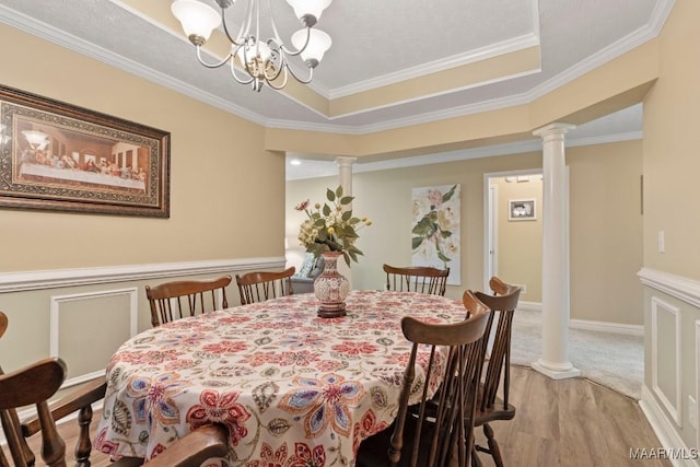 dining space featuring crown molding, a raised ceiling, a notable chandelier, light wood-style floors, and ornate columns