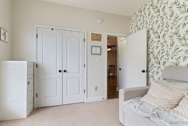 bedroom featuring a closet, an accent wall, baseboards, wallpapered walls, and light colored carpet