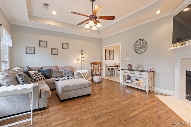 living room with a high end fireplace, a ceiling fan, a tray ceiling, and wood finished floors