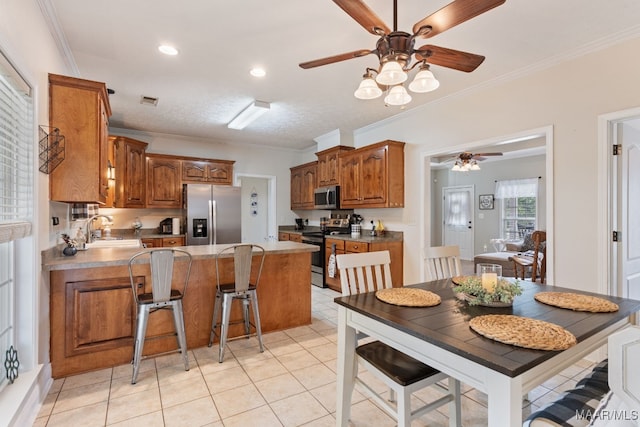 kitchen featuring ceiling fan, brown cabinetry, appliances with stainless steel finishes, a sink, and a peninsula