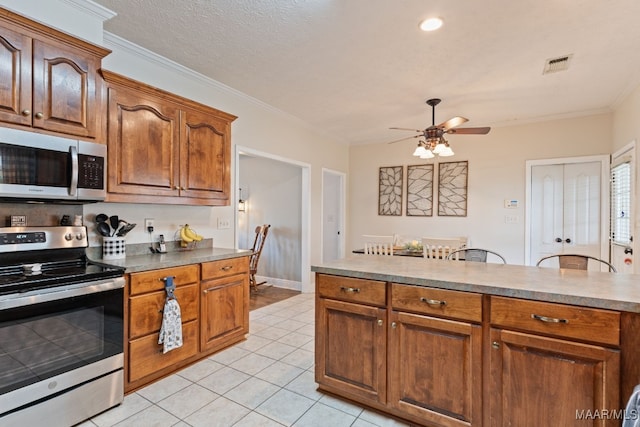 kitchen with light tile patterned flooring, ceiling fan, appliances with stainless steel finishes, visible vents, and ornamental molding