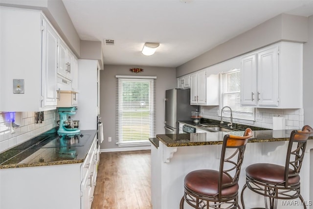 kitchen featuring a kitchen bar, visible vents, a sink, a peninsula, and under cabinet range hood