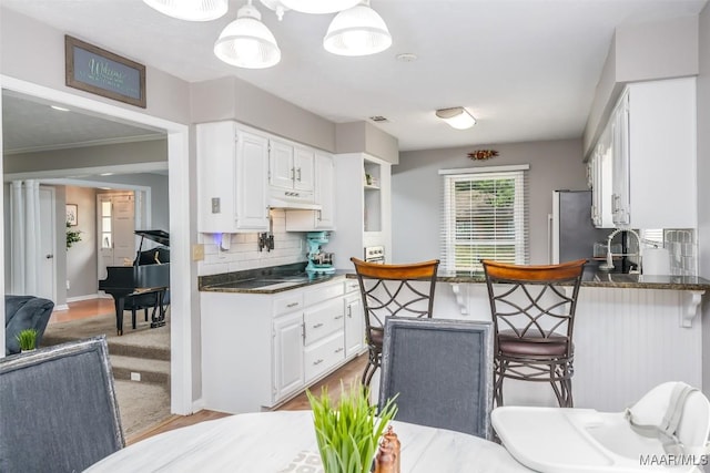 kitchen featuring freestanding refrigerator, white cabinetry, a kitchen breakfast bar, and dark countertops