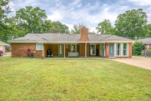 back of property with fence, a patio, a chimney, brick siding, and a lawn
