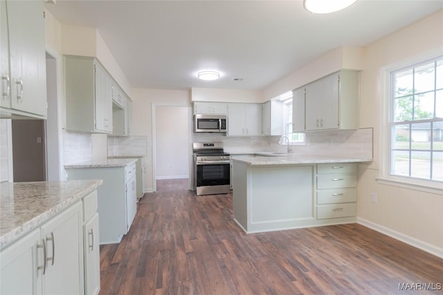 kitchen featuring decorative backsplash, dark wood finished floors, a sink, a peninsula, and stainless steel appliances