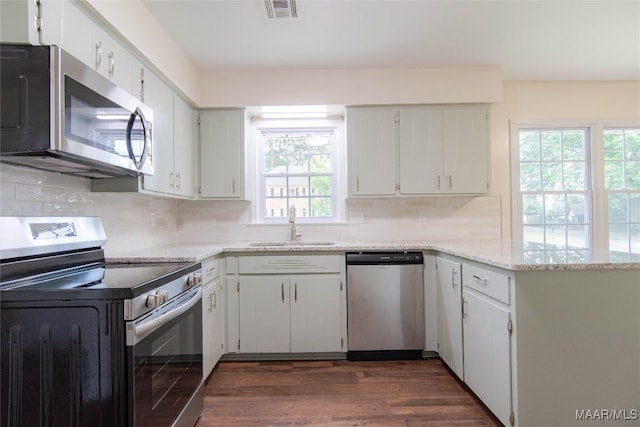 kitchen with appliances with stainless steel finishes, a sink, a peninsula, decorative backsplash, and visible vents