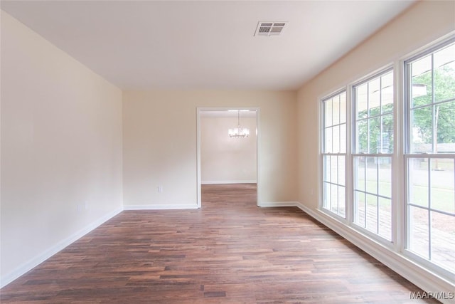 unfurnished room with an inviting chandelier, baseboards, dark wood-style flooring, and visible vents