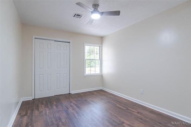 unfurnished bedroom with dark wood-style flooring, a textured ceiling, visible vents, baseboards, and a closet
