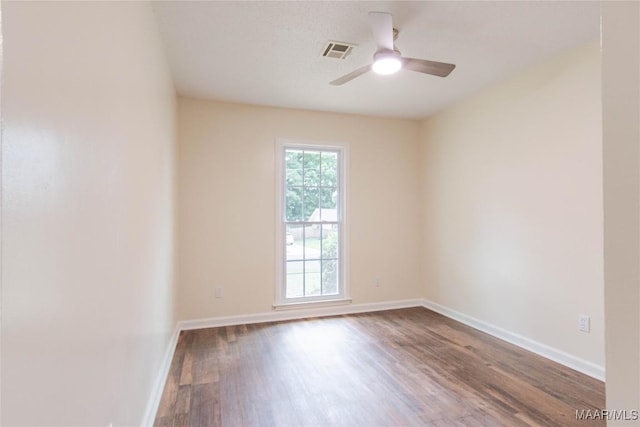 empty room featuring dark wood-type flooring, a ceiling fan, baseboards, and visible vents