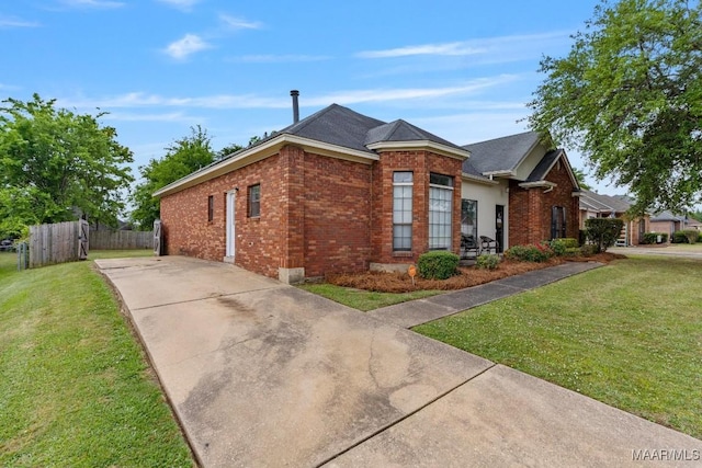 view of property exterior featuring a lawn, fence, driveway, and brick siding