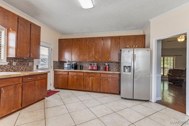 kitchen featuring brown cabinetry, backsplash, appliances with stainless steel finishes, light countertops, and ornamental molding