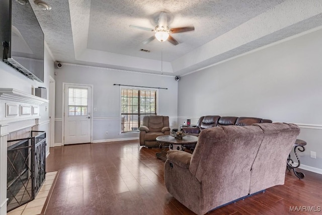 living area with a raised ceiling, a ceiling fan, a textured ceiling, and wood finished floors