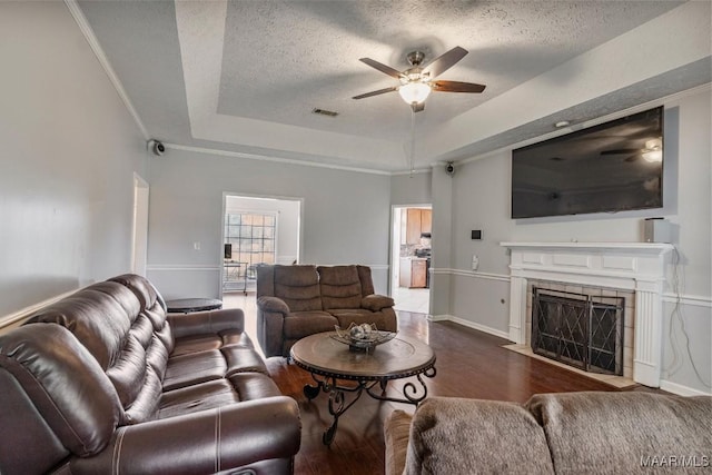 living area with ceiling fan, a fireplace, a textured ceiling, wood finished floors, and a tray ceiling