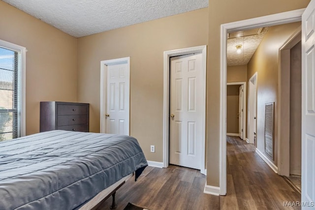 bedroom with attic access, dark wood-style flooring, a textured ceiling, visible vents, and baseboards