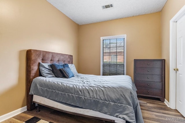 bedroom with a textured ceiling, baseboards, visible vents, and wood finished floors