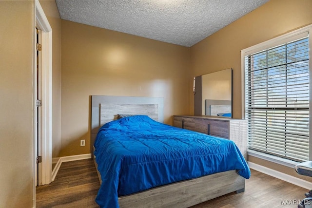 bedroom featuring baseboards, a textured ceiling, and wood finished floors