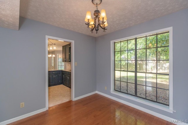 unfurnished room featuring baseboards, a wealth of natural light, wood finished floors, and a chandelier