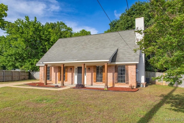 view of front facade featuring fence, a front lawn, brick siding, a chimney, and covered porch