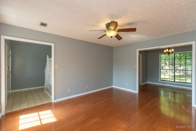 unfurnished room featuring visible vents, wood finished floors, baseboards, a textured ceiling, and ceiling fan with notable chandelier